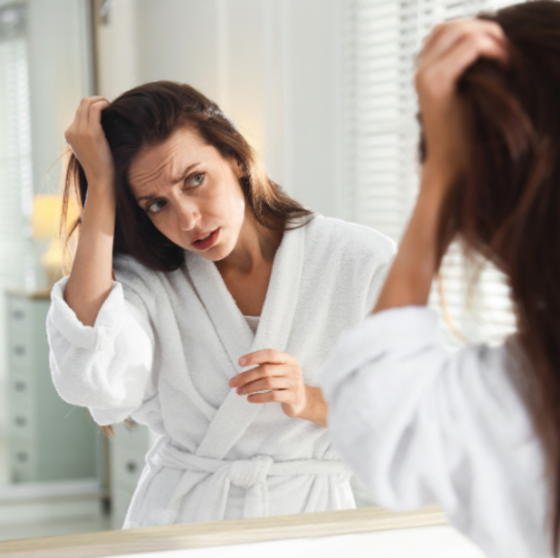 Woman in a white robe adjusting her hair in front of a mirror.